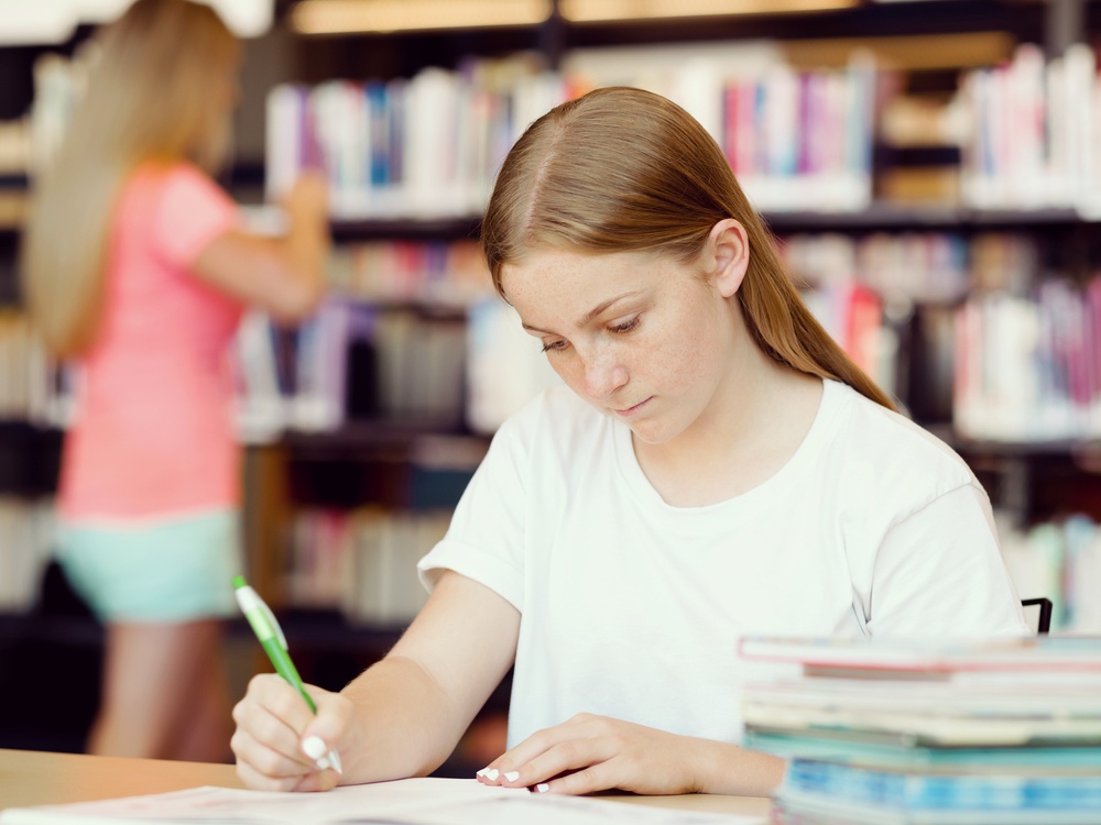 Teenage girl with books studying in library